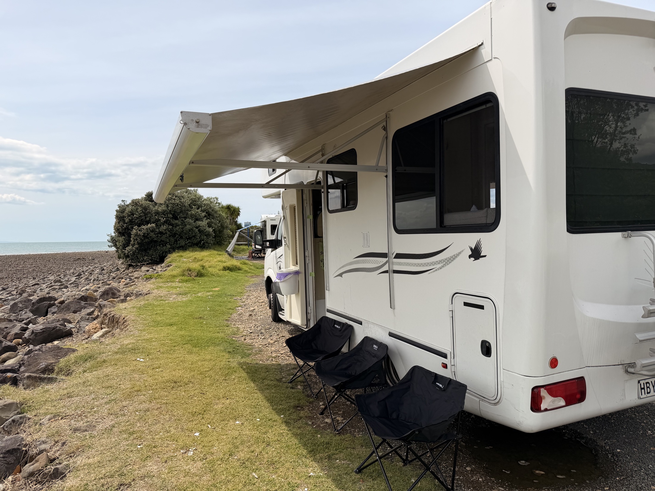 The real Hey Buddy motorhome with its awning open beside a New Zealand beach